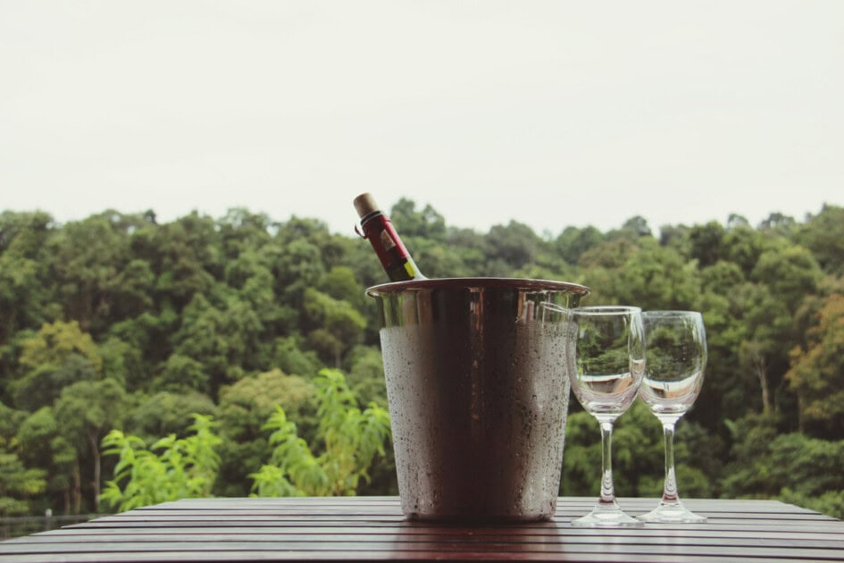 Ice bucket with wine and 2 glasses beside it on a table